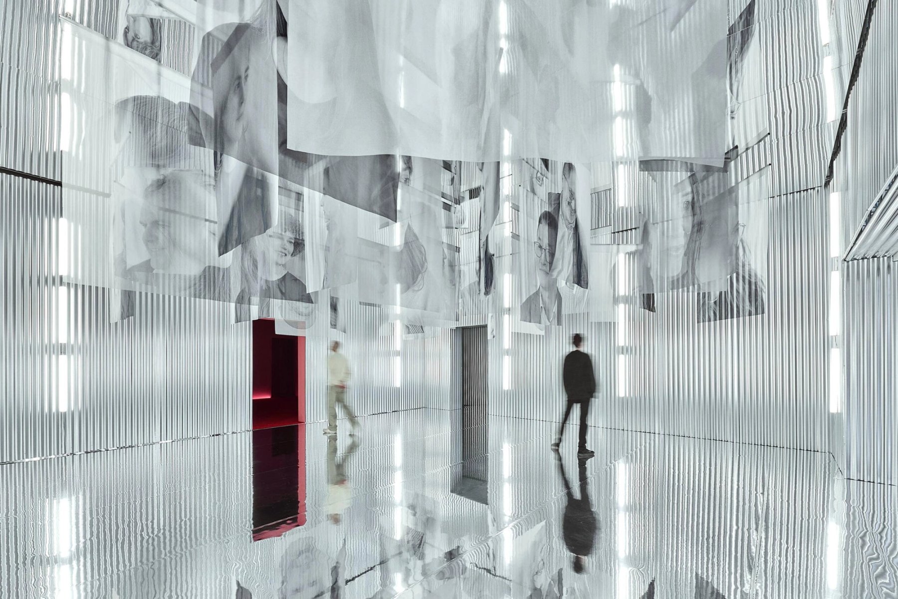 A mirrored room hung with printed sheets, a figure standing among them.