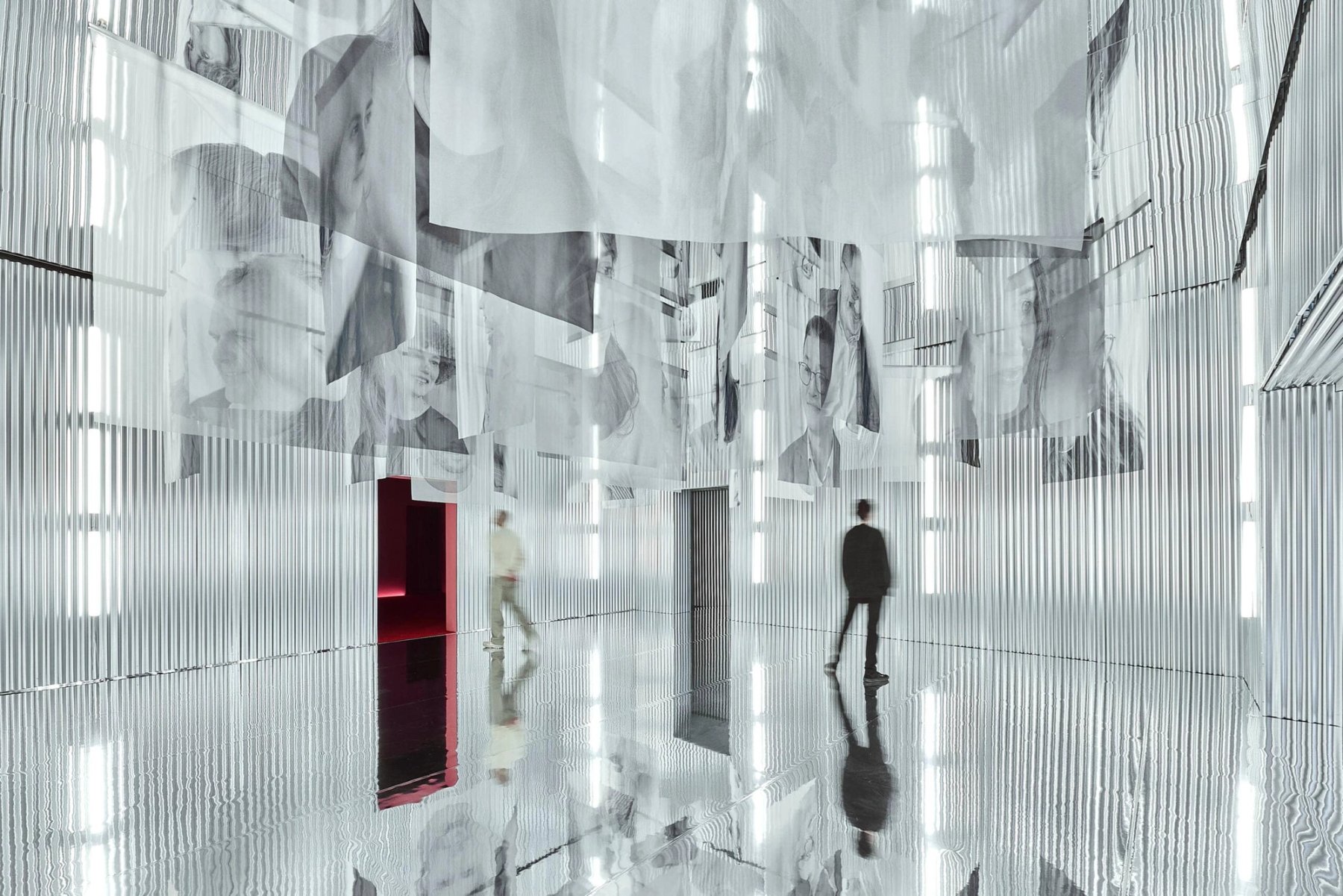 A mirrored room hung with printed sheets, a figure standing among them.
