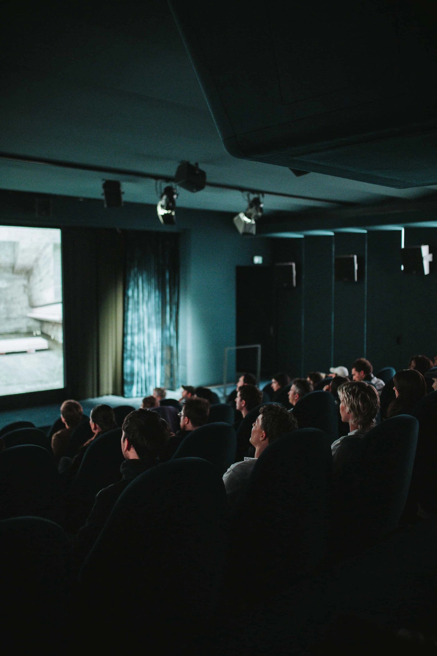 An audience watches a film in a small cinema, the screen lighting their faces.