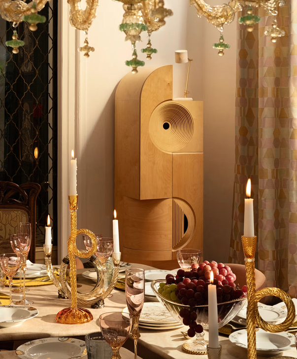 A wooden cabinet beside a dinner table laid with candles, glasses and a bowl of grapes.
