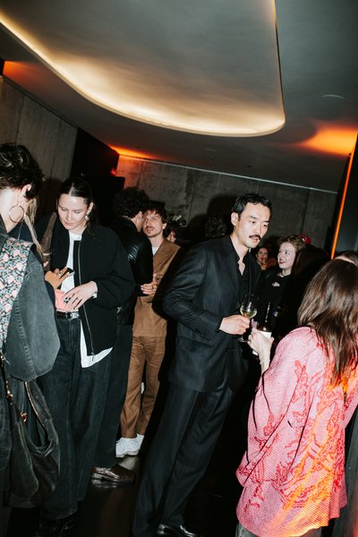 Guests with drinks at a party, standing under a lit ceiling.