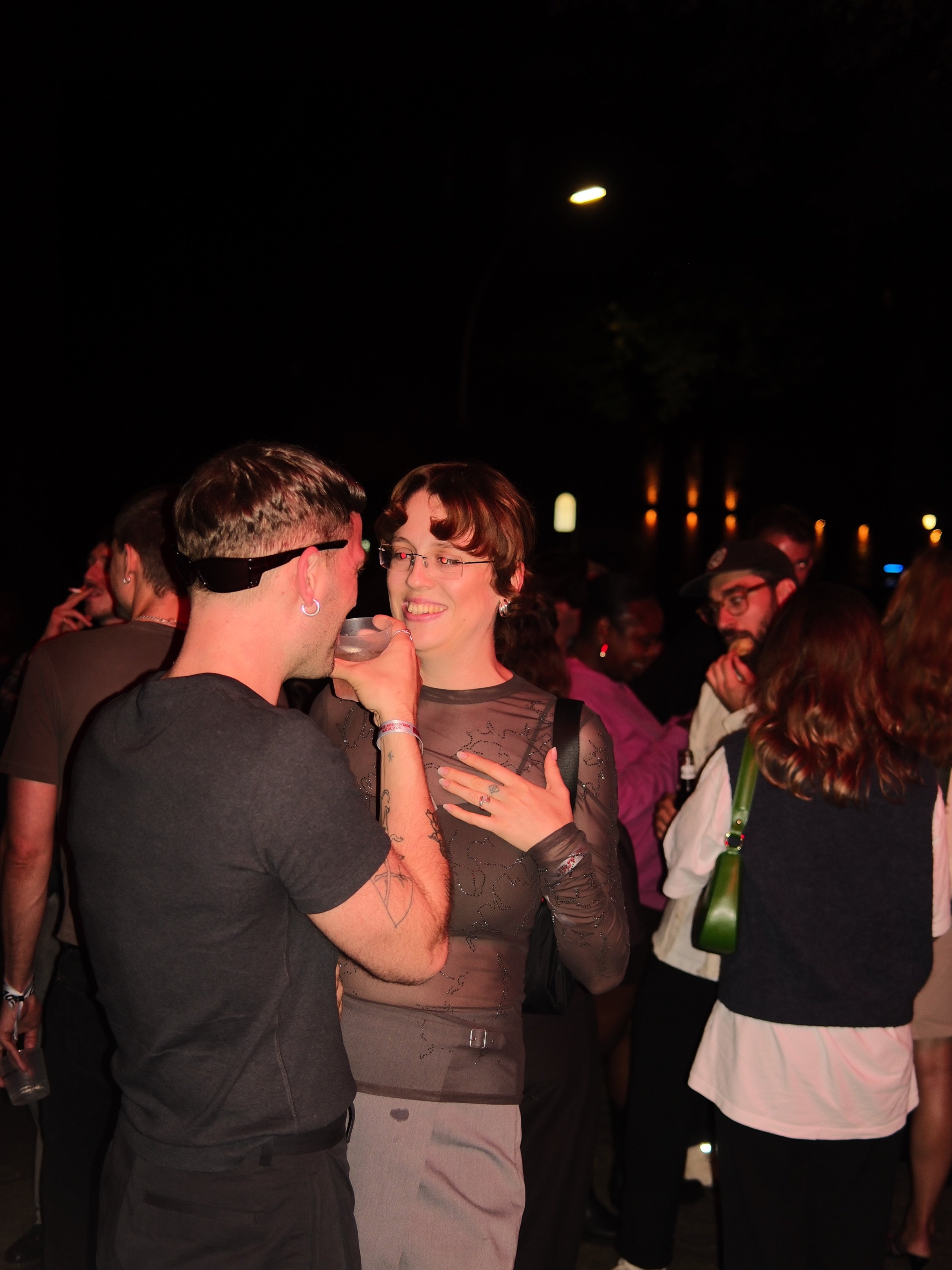 Guests talk and drink outside at night, lit by a camera flash.
