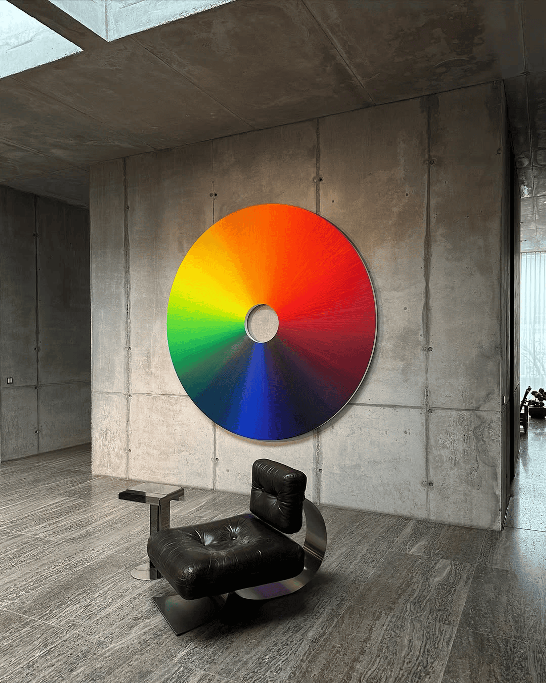 A colour wheel painting on a concrete wall, with a black leather chair below it.