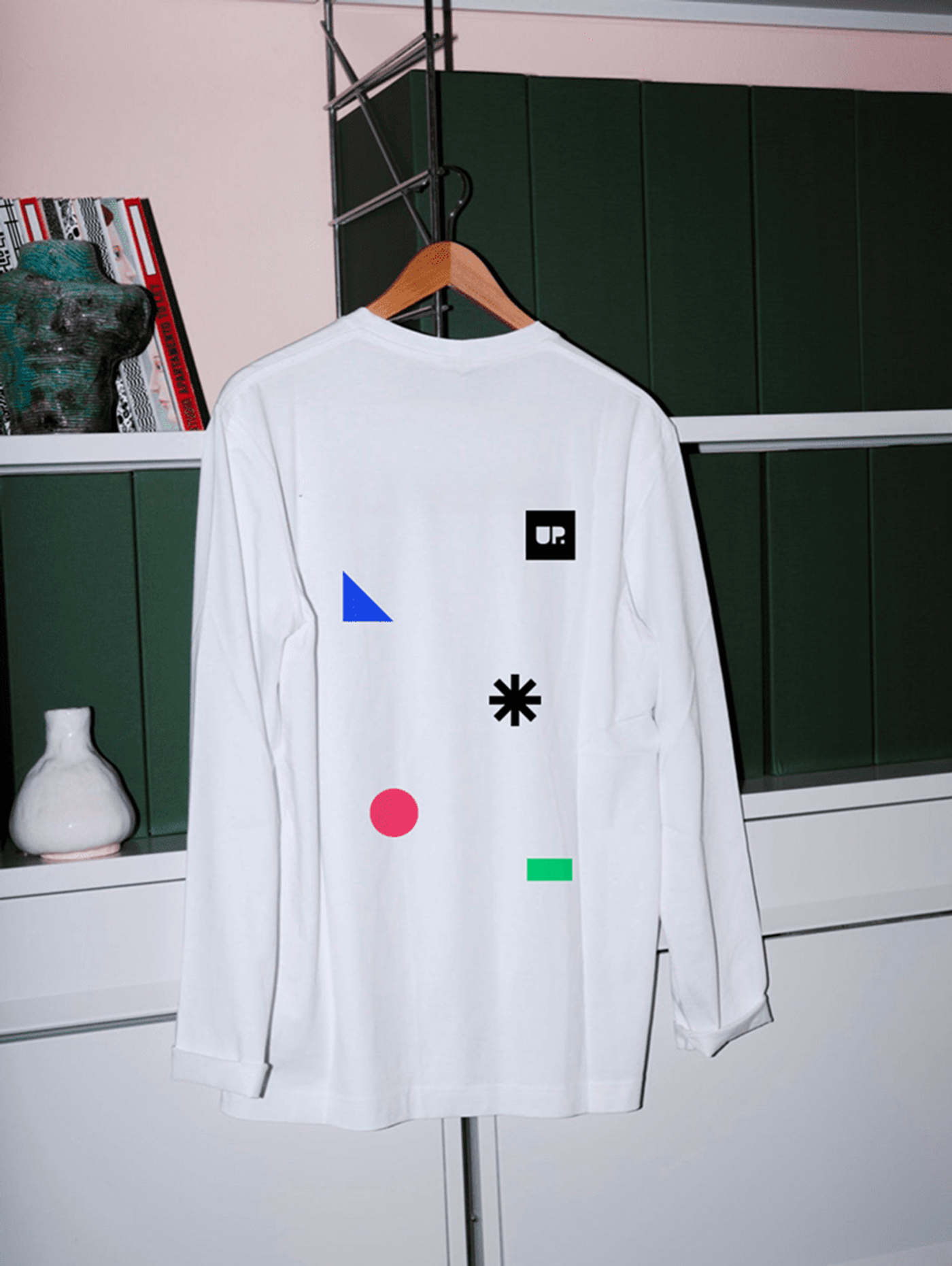 A white long sleeved shirt on a hanger, printed with the UP GREAT shapes.