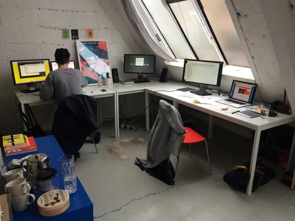 An attic studio with two people working at desks under a sloped window.