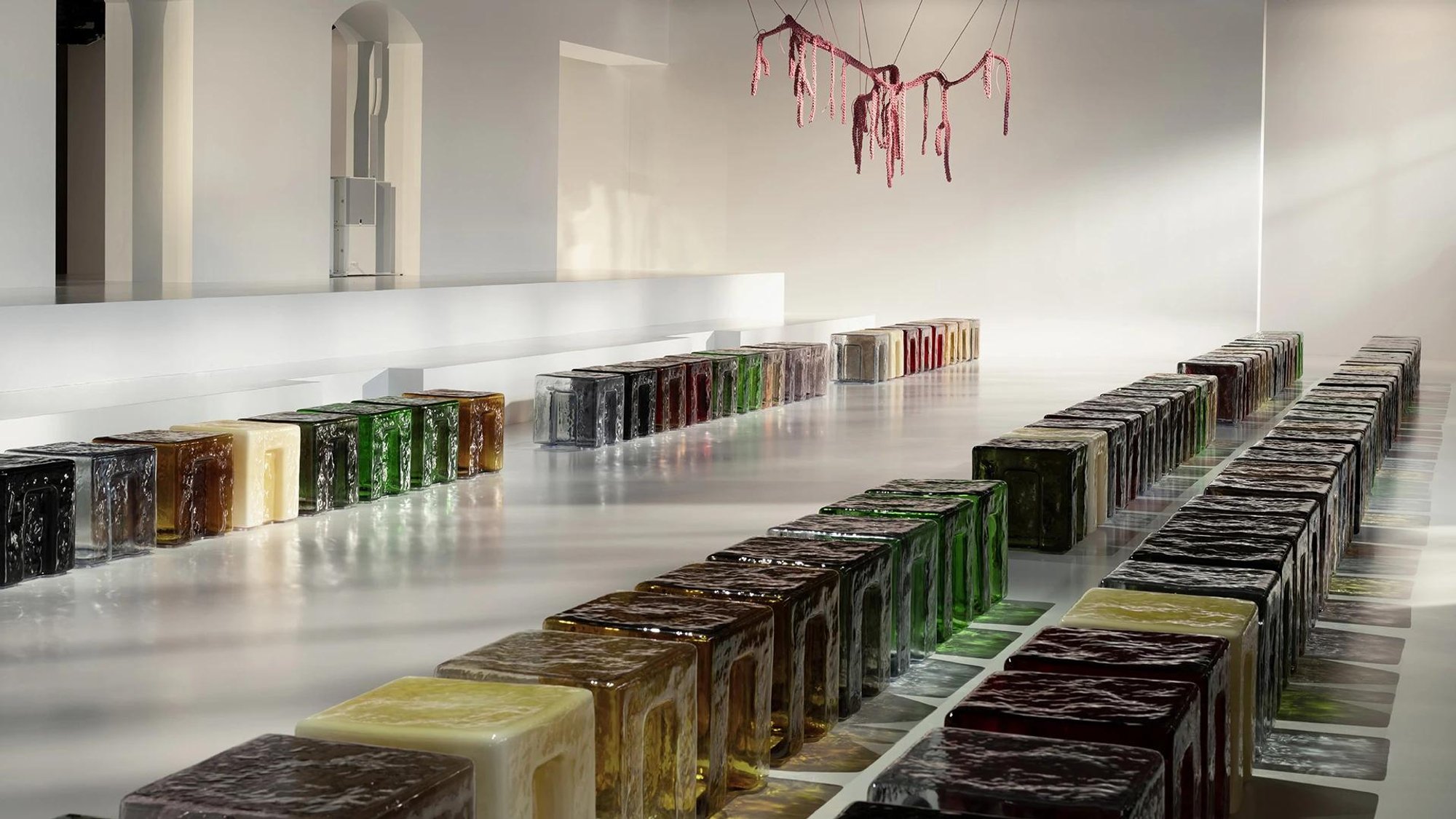 A long line of coloured cast glass blocks along the floor of a white gallery.