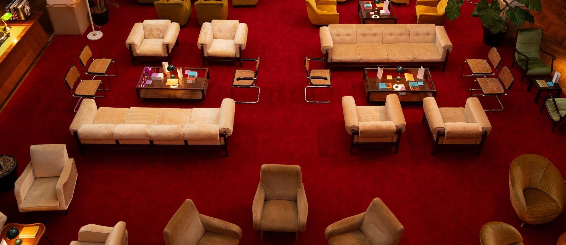 A red carpeted lounge seen from above, with cream sofas and low tables between them.
