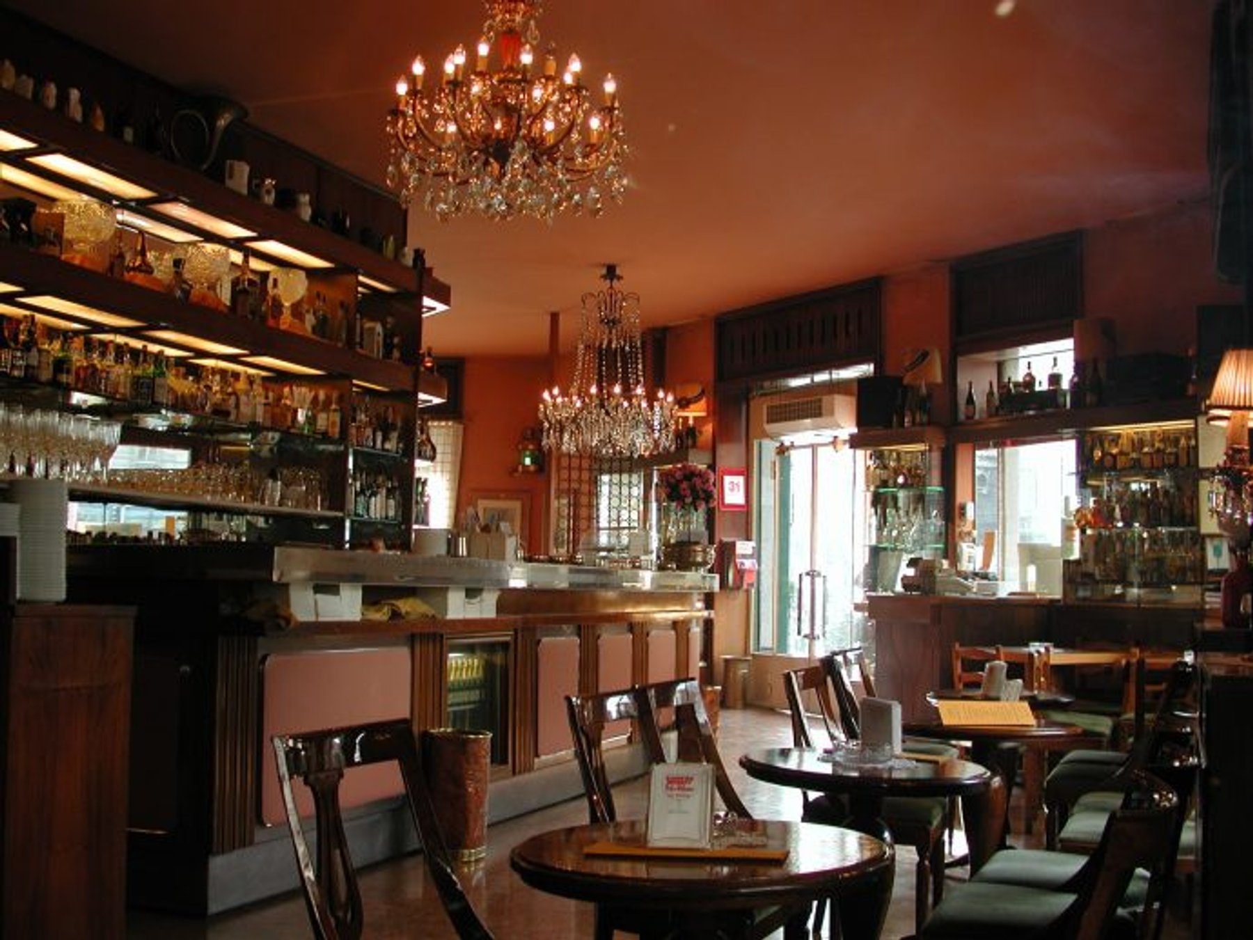 The inside of Bar Basso, with chandeliers over the tables and bottles along the back wall.
