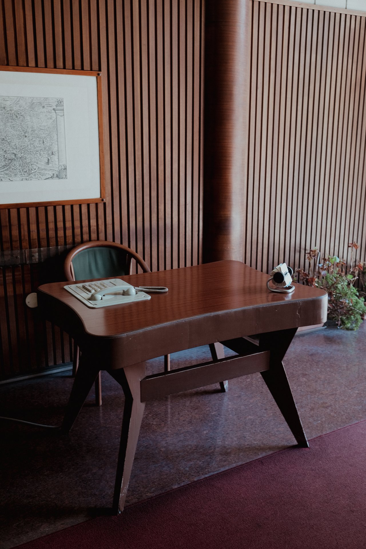 A wooden desk with a telephone on it, in front of a slatted wood wall.