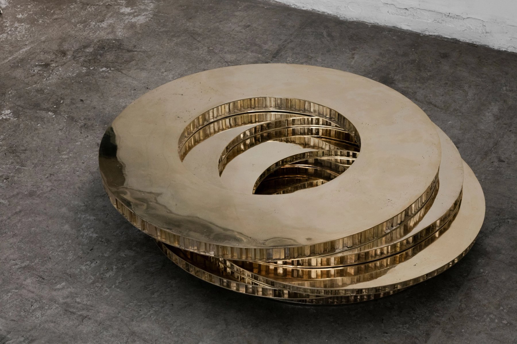 A spiral dish of polished brass, lying on a concrete floor.
