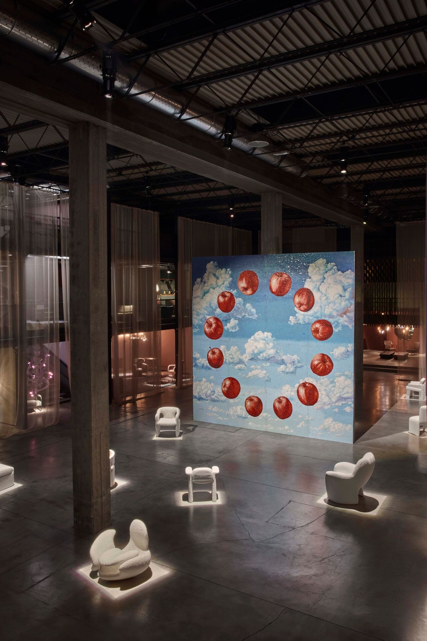 An exhibition hall with a painted sky of apples, white chairs lit around it.