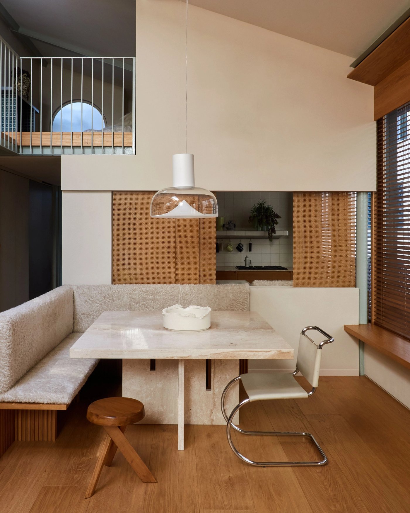 A dining nook with a stone table, a built in bench and a glass pendant above it.