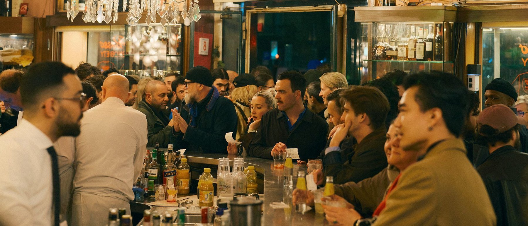 A crowded bar, drinkers standing three deep along the counter.