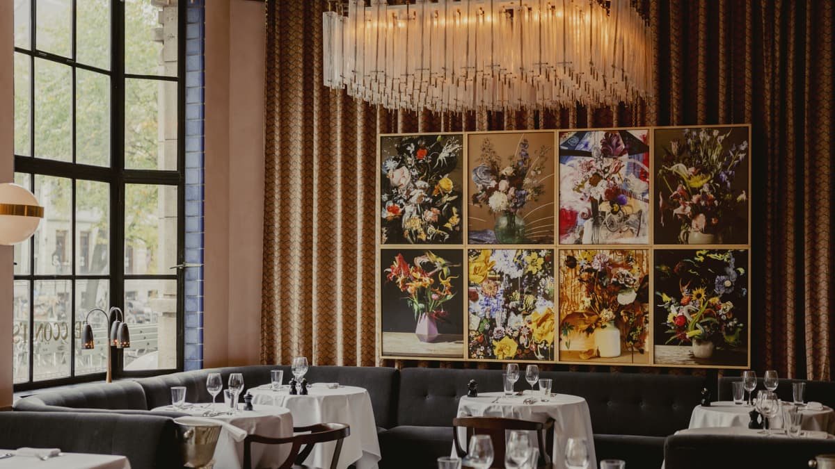 A restaurant with a long crystal chandelier and a wall of flower paintings.