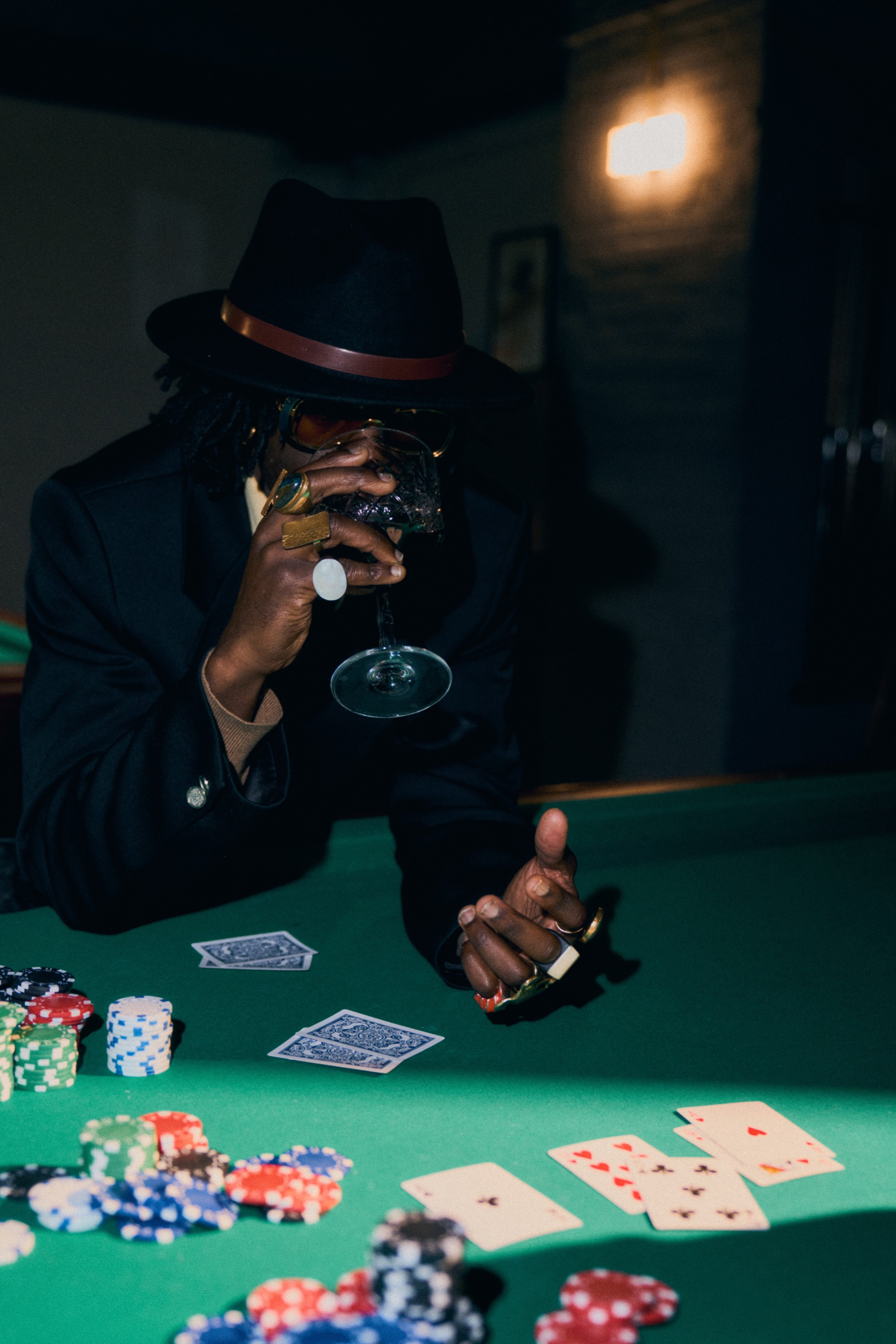 A man in a hat sips from a wine glass at a poker table.