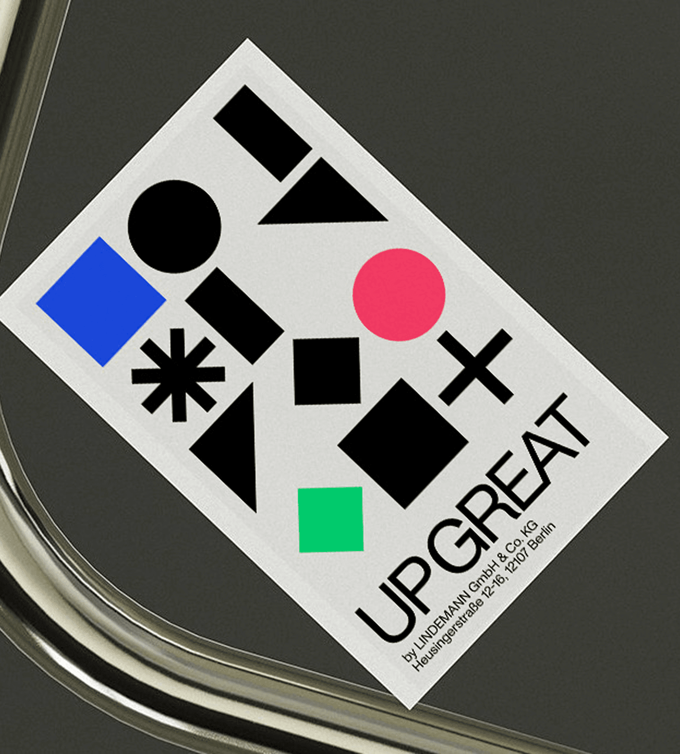 A sticker printed with the UP GREAT shapes, lying on brushed metal.