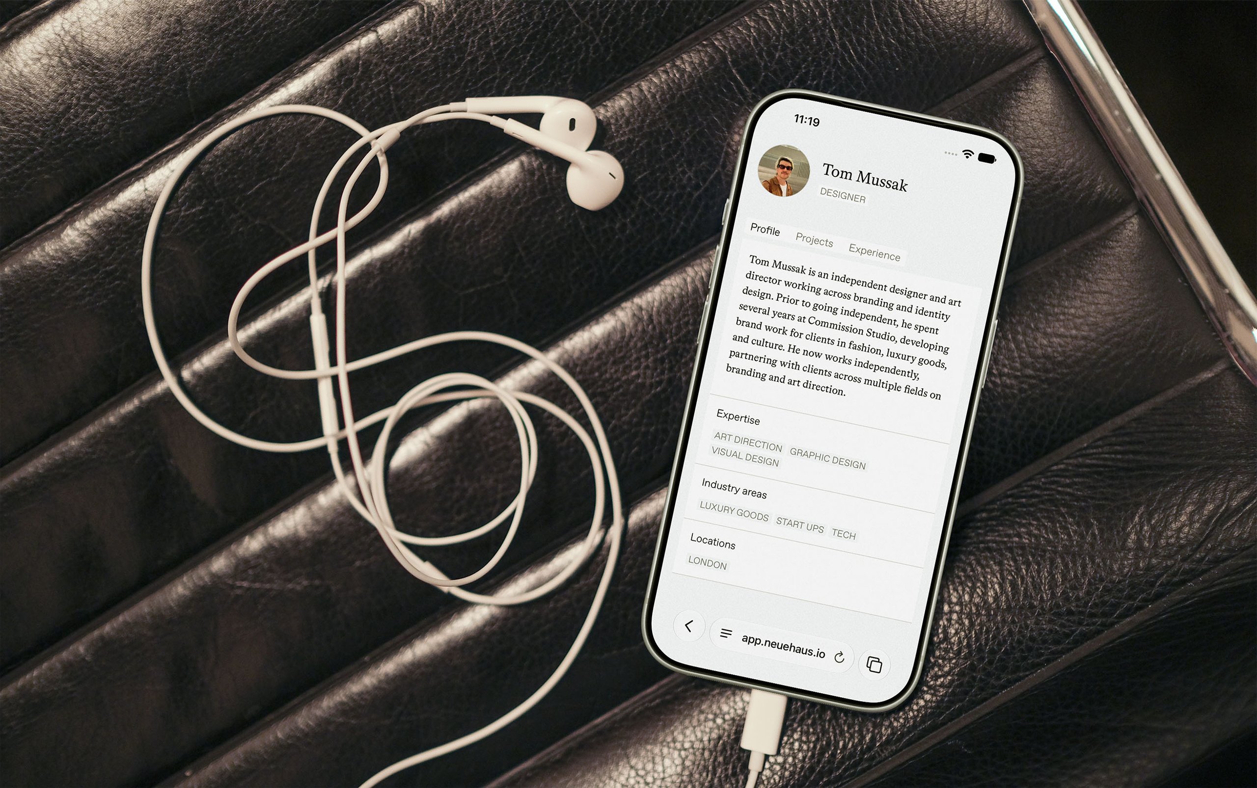 A phone showing a member profile, lying on a leather seat with earphones beside it.