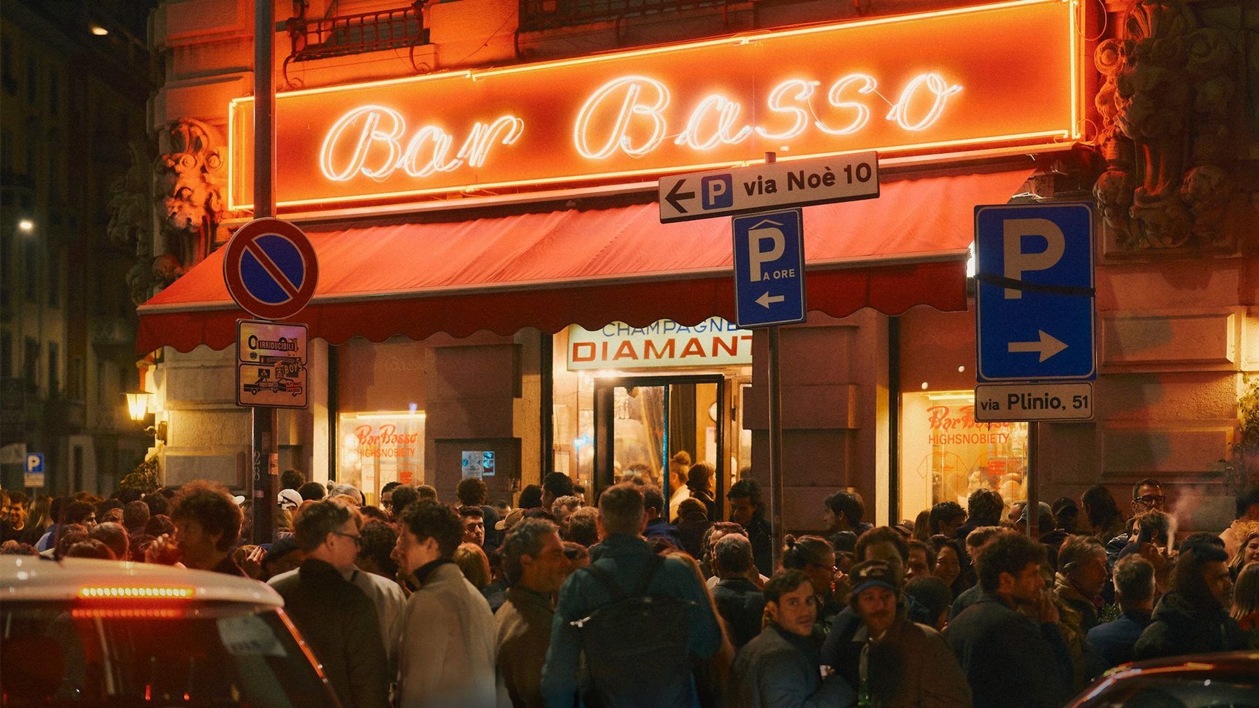 The Bar Basso neon sign at night, with a crowd on the pavement below it.