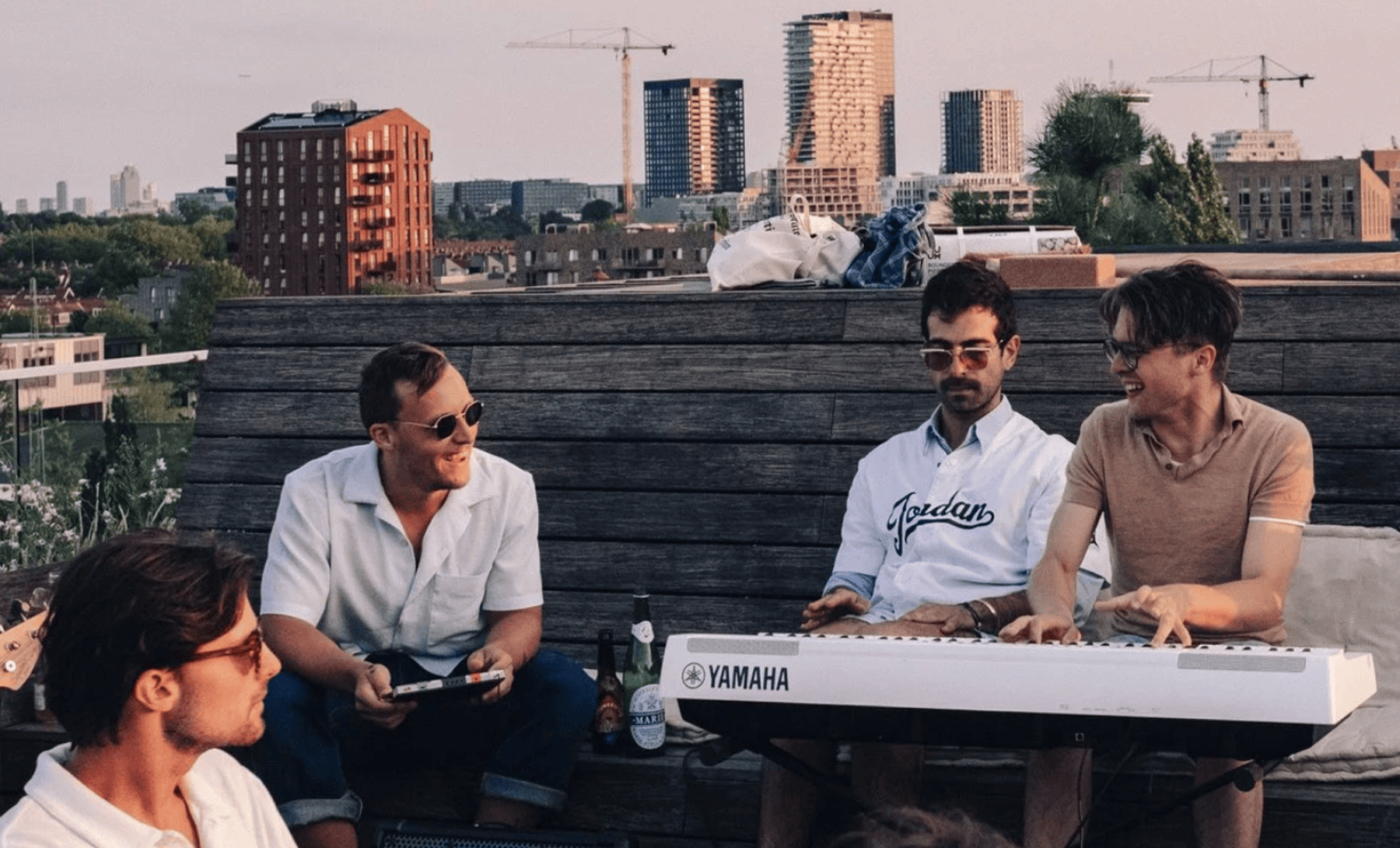 Friends on a rooftop at sunset, one of them playing a keyboard.