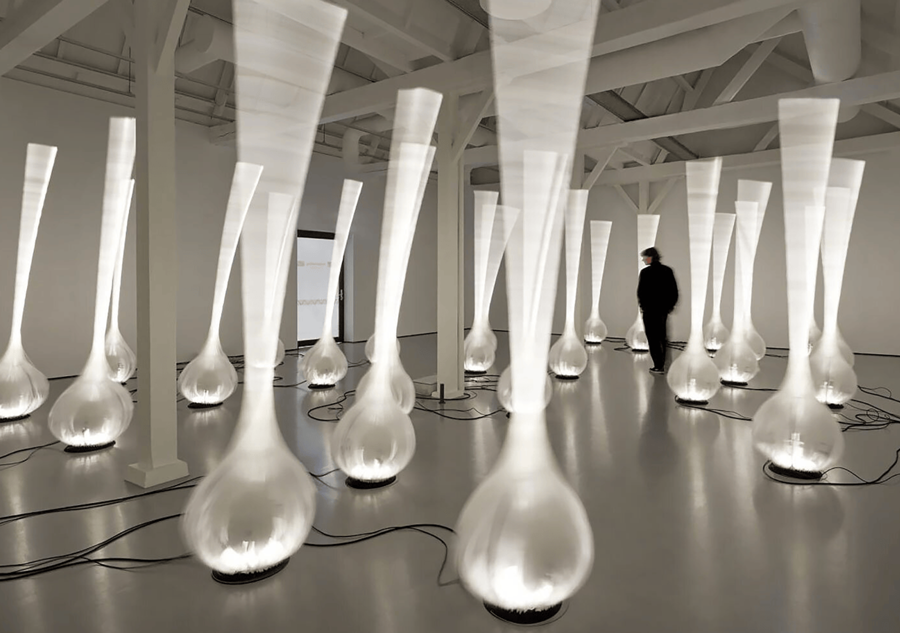 A hall filled with lit inflatable drop shapes, a figure walking between them.