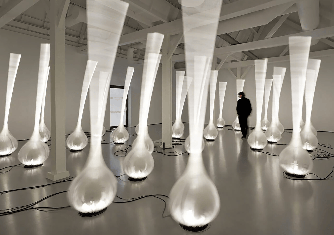 A hall filled with lit inflatable drop shapes, a figure walking between them.