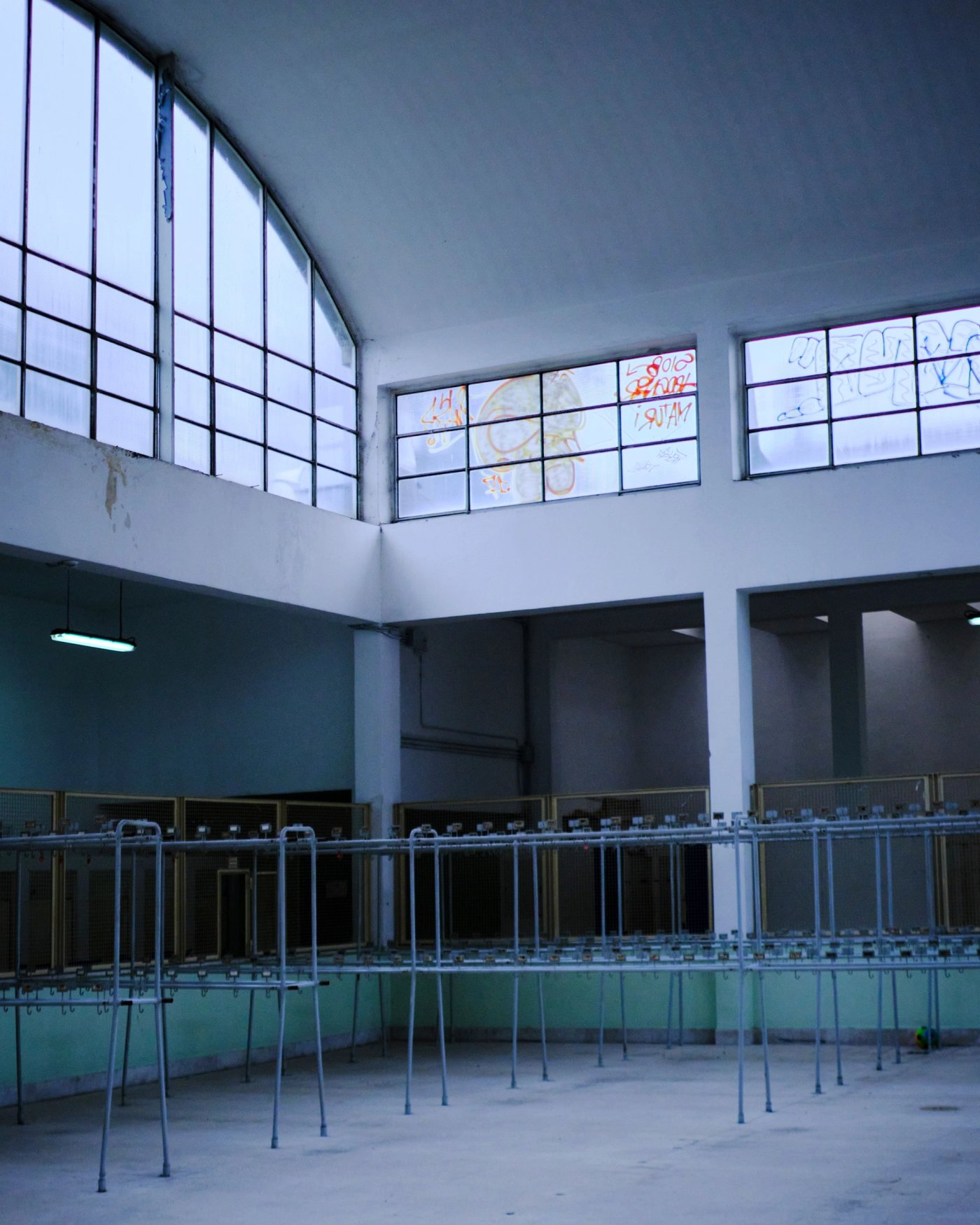 A glass factory hall in Murano, with arched windows and empty racks along the walls.