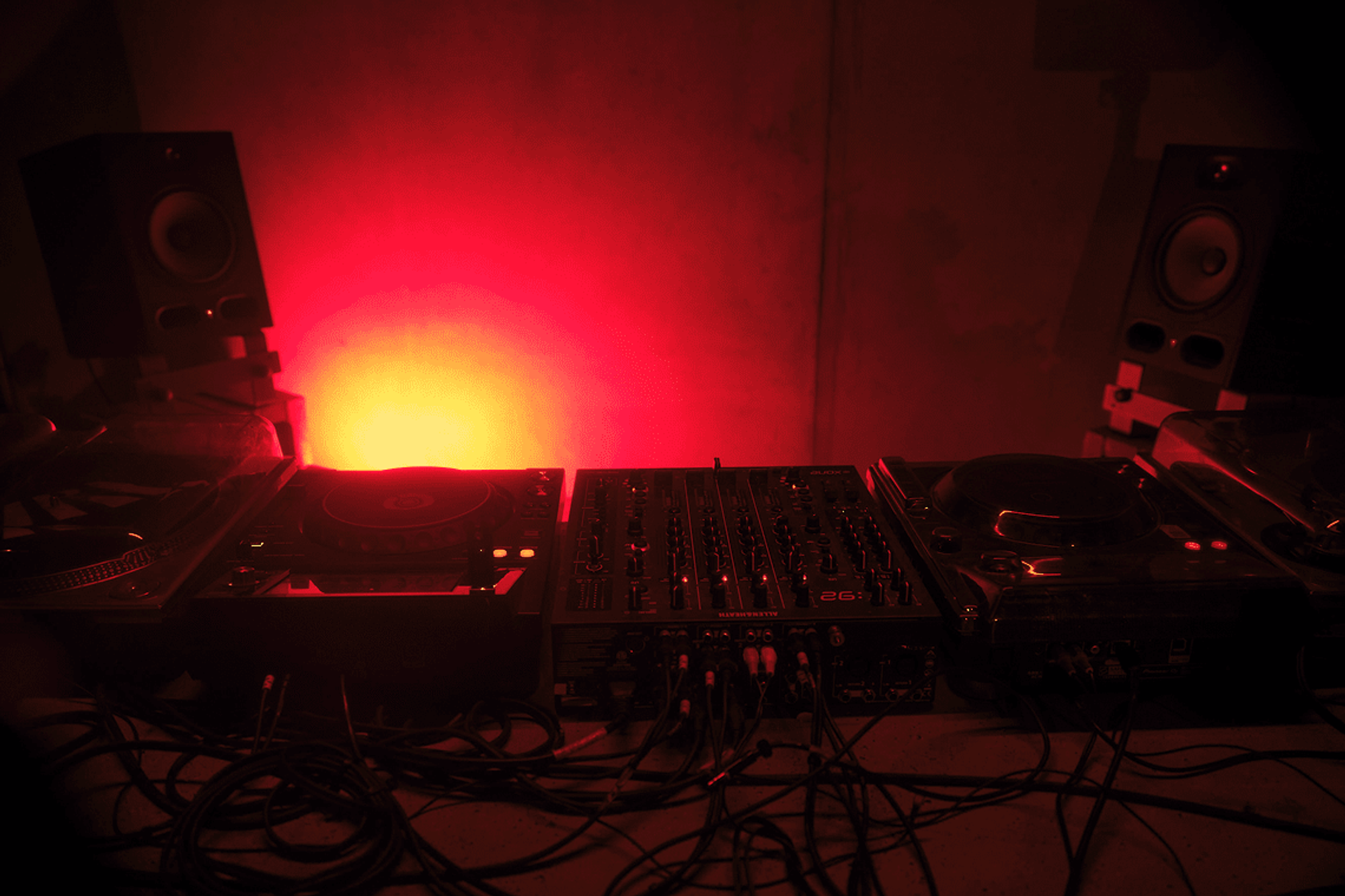 A mixer and monitor speakers in a booth, lit red from behind.