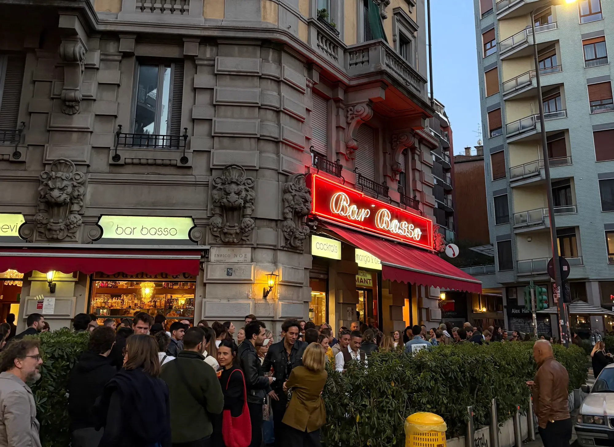 The corner of Bar Basso at dusk, people standing outside with drinks.