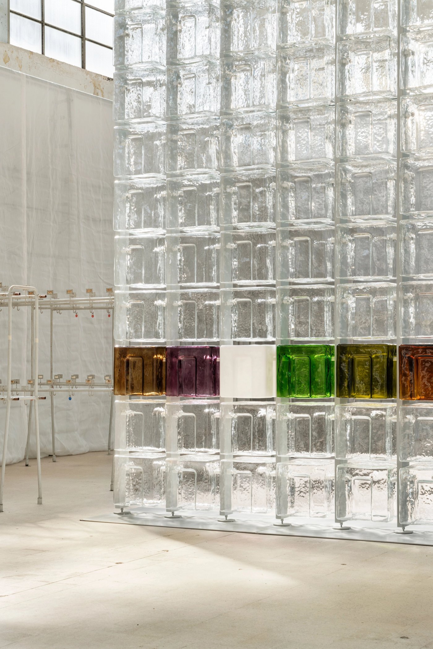 A wall of clear glass bricks in a factory, with a band of coloured ones across the middle.