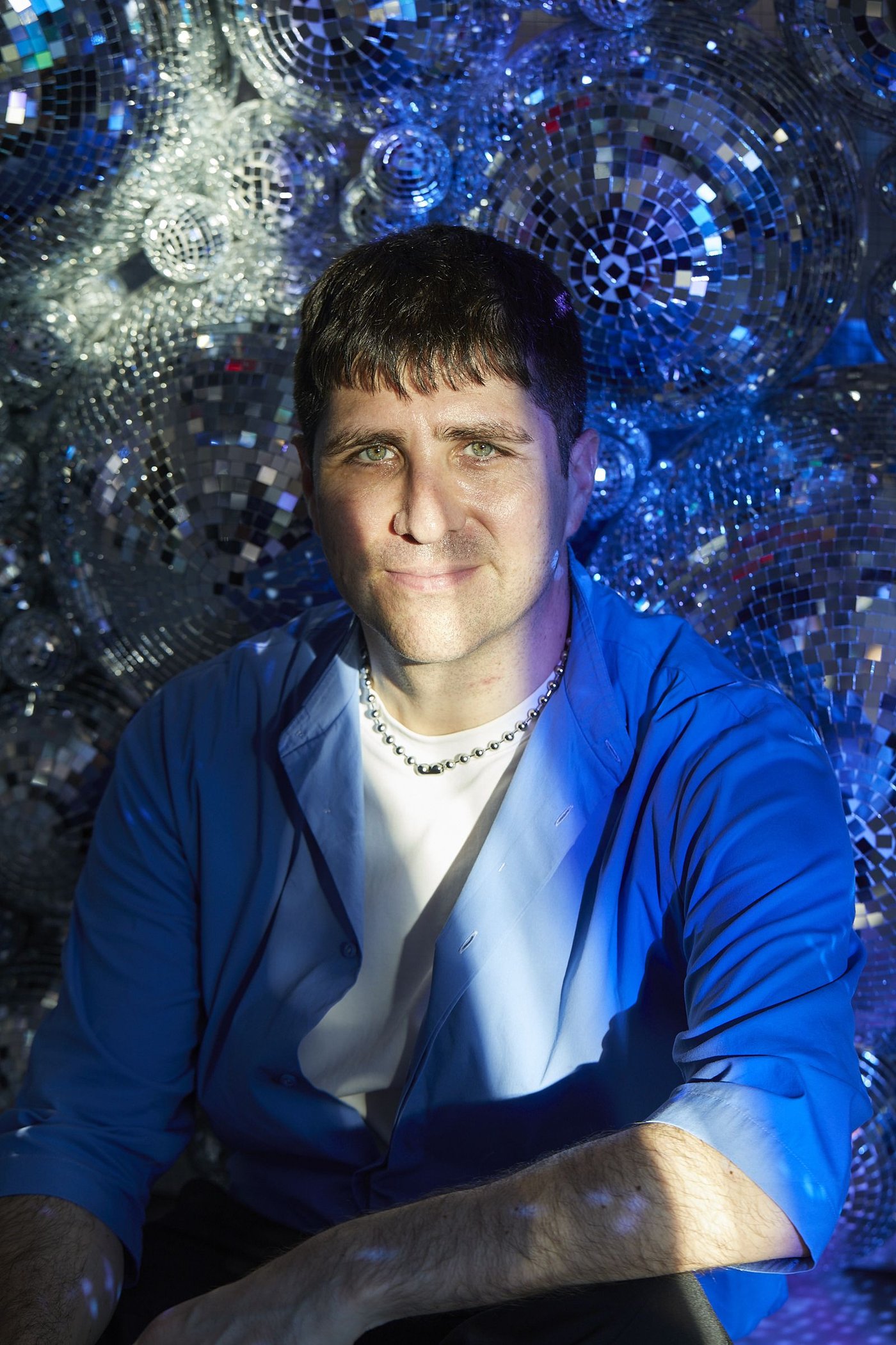 A portrait of a man in a blue jacket in front of a wall of mirror balls.
