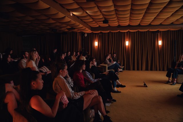 A cinema room full with audience and speakers sitting on the stage