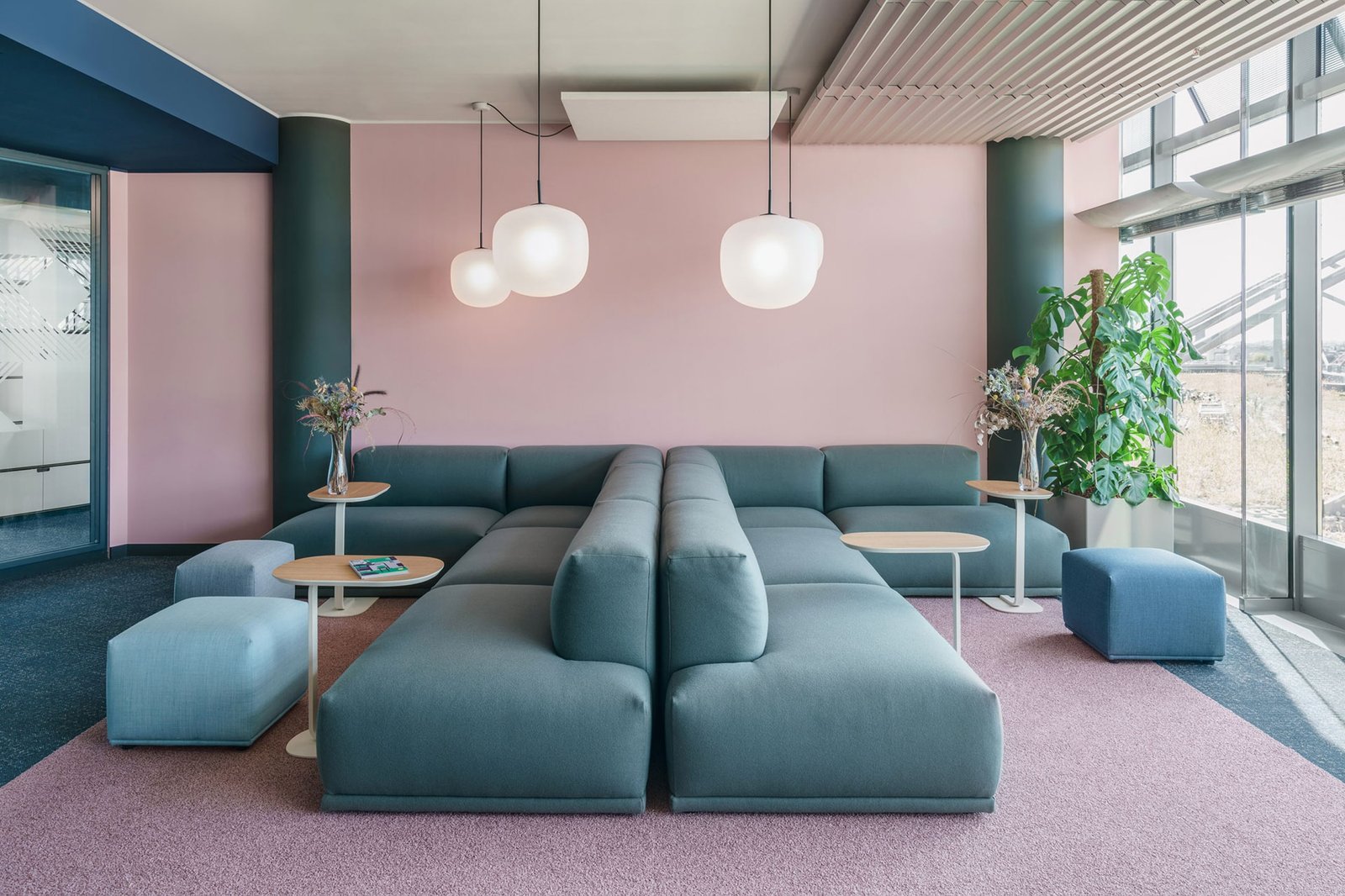 A lounge with blue sofas on a pink carpet, under paper globe lights.