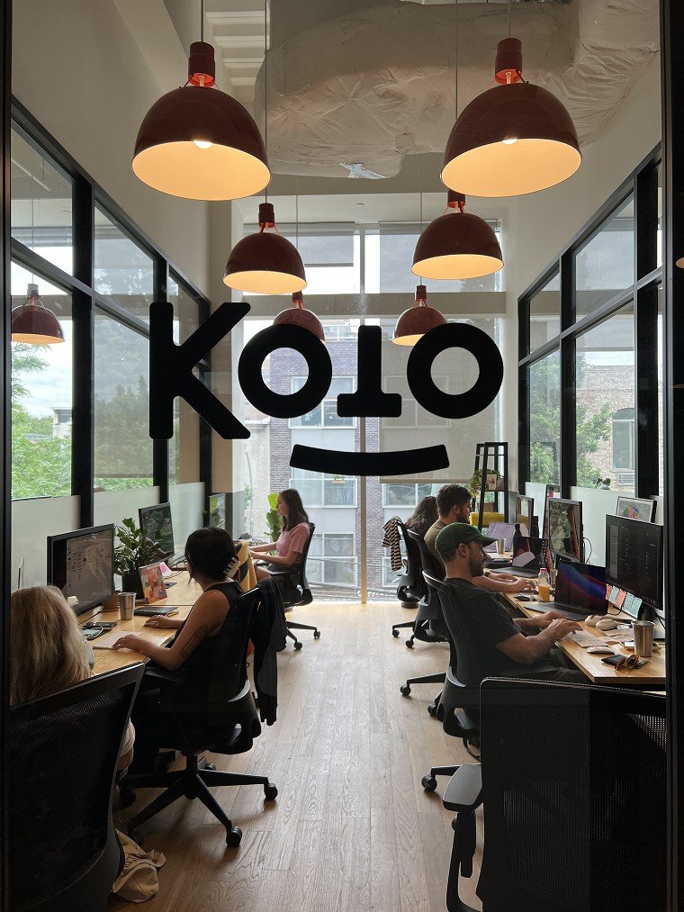 The Koto studio, with the studio mark on the glass wall and the team at their desks.