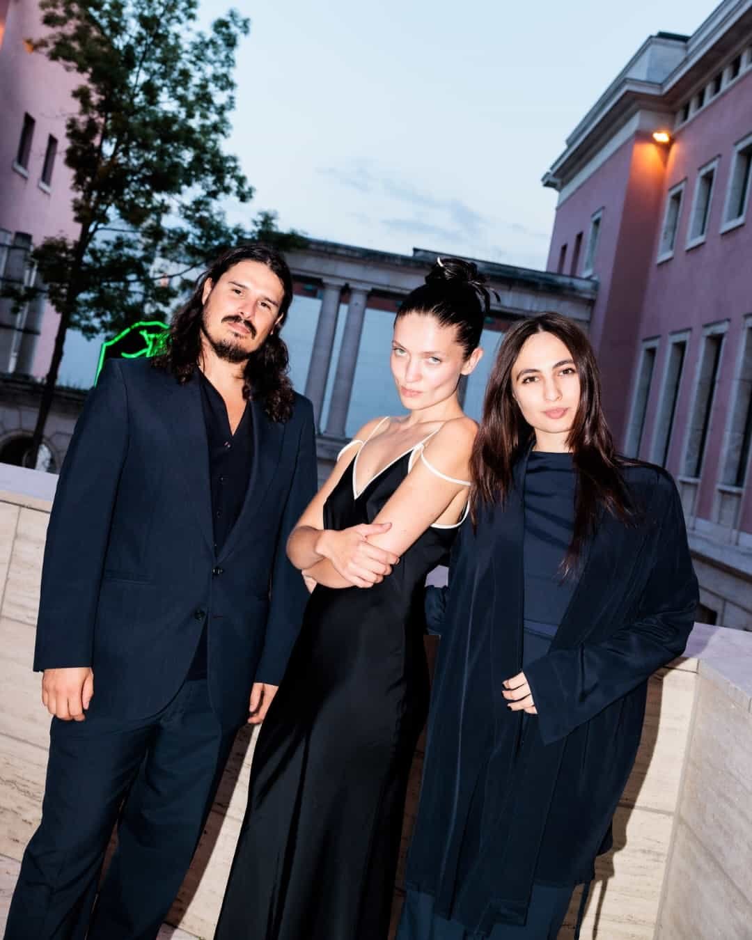 Three guests in black stand outside a pink building at dusk during art week.