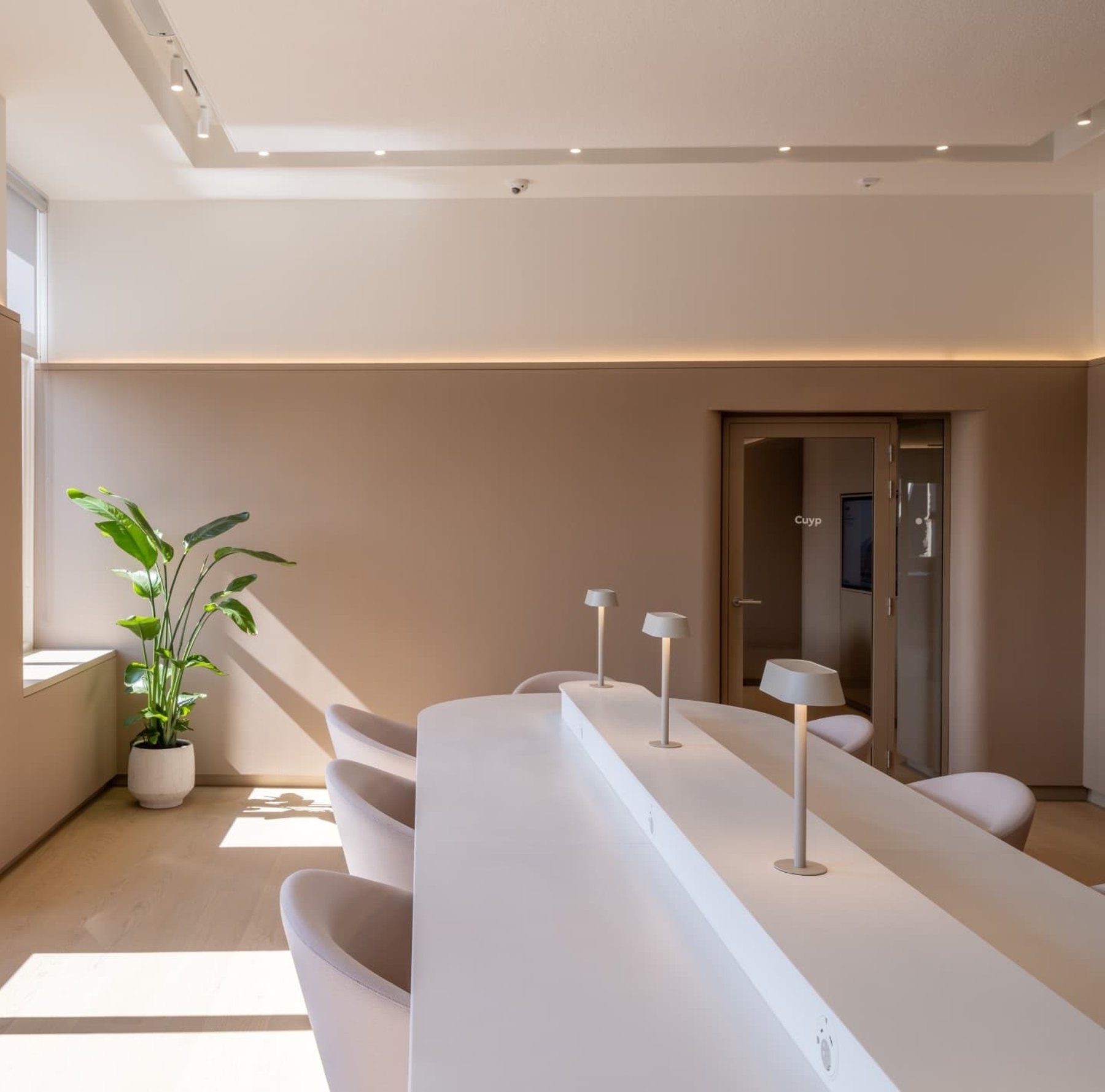 A pale reception counter with stools along it, under soft cove lighting.