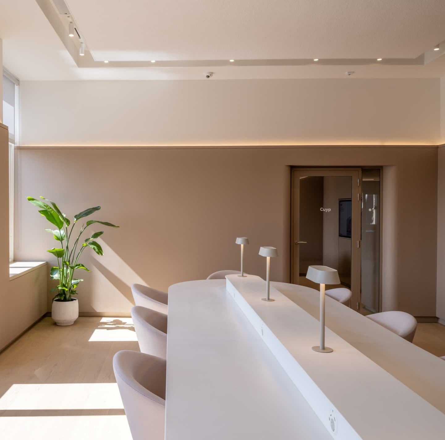 A pale reception counter with stools along it, under soft cove lighting.