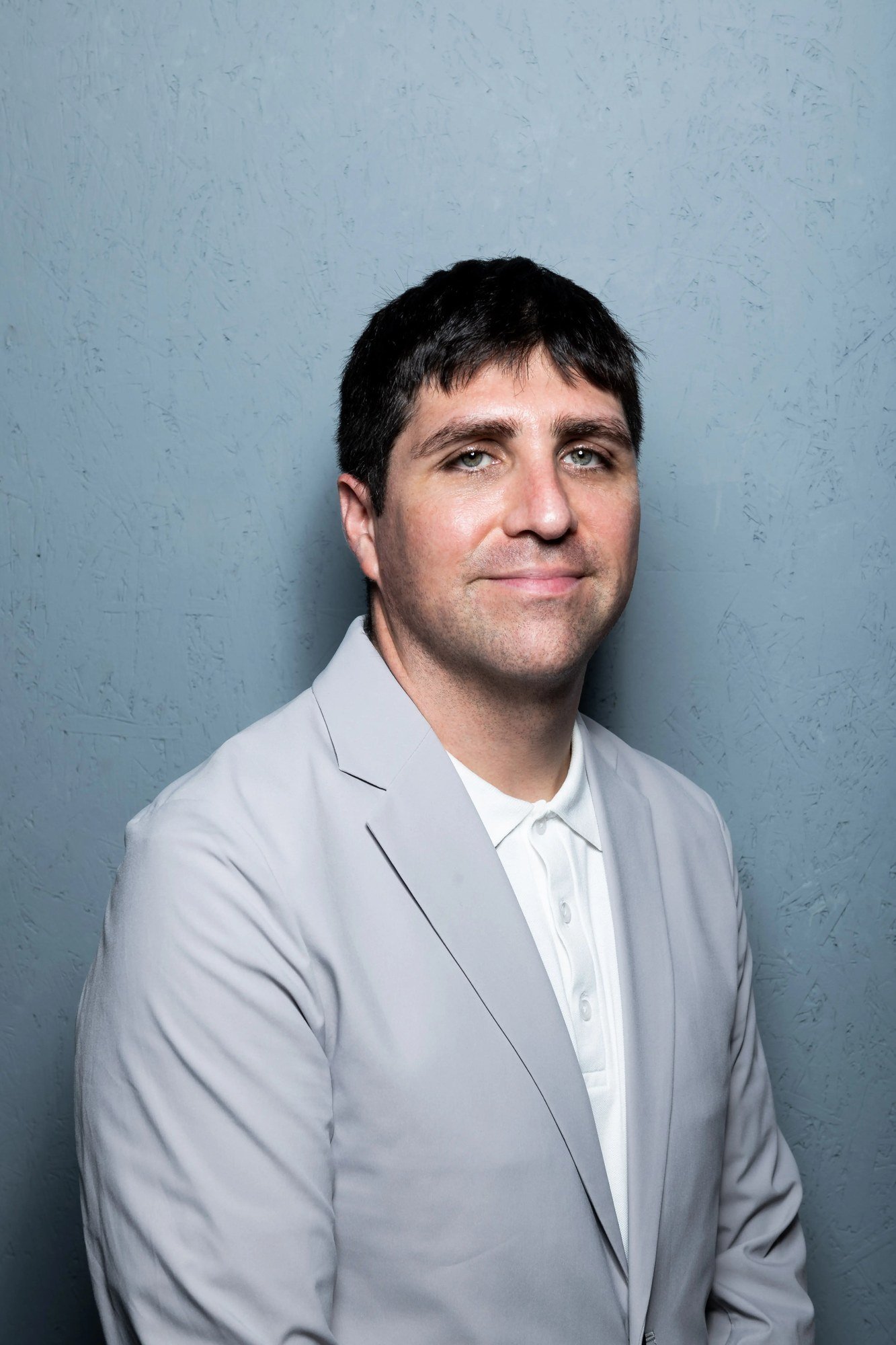 A portrait of a man in a grey suit against a blue wall.