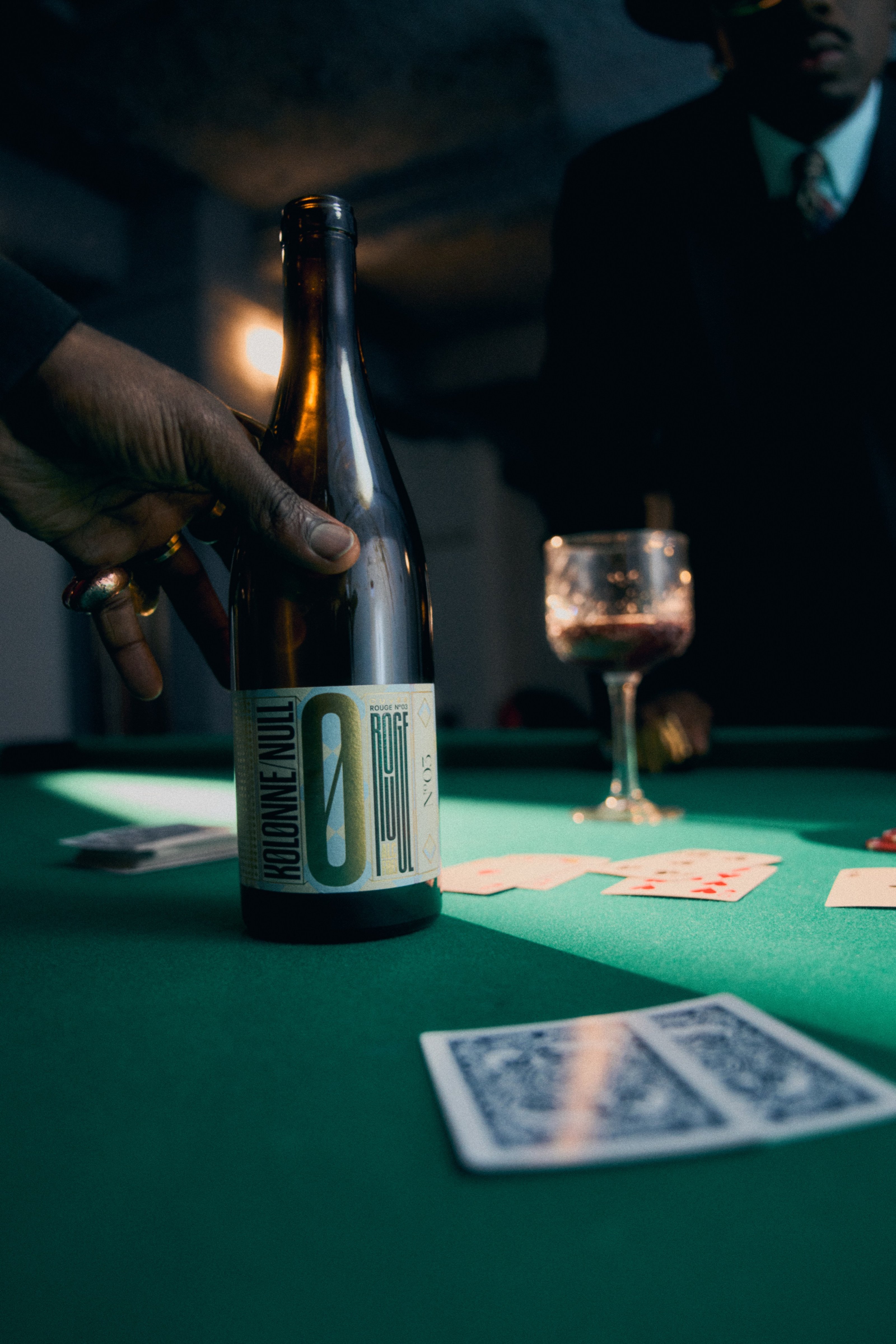 A bottle of Kolonne Null and a glass on a green table, a man in a suit standing behind.
