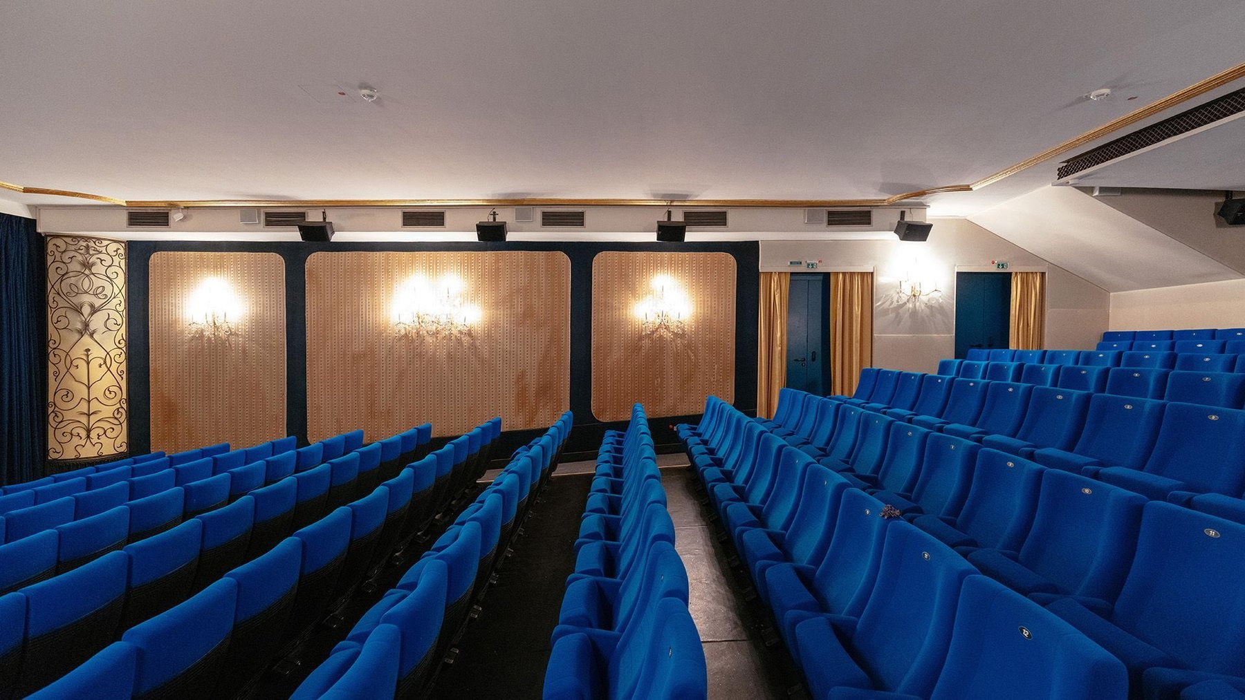 A cinema with rows of blue velvet seats and wooden panels along the walls.