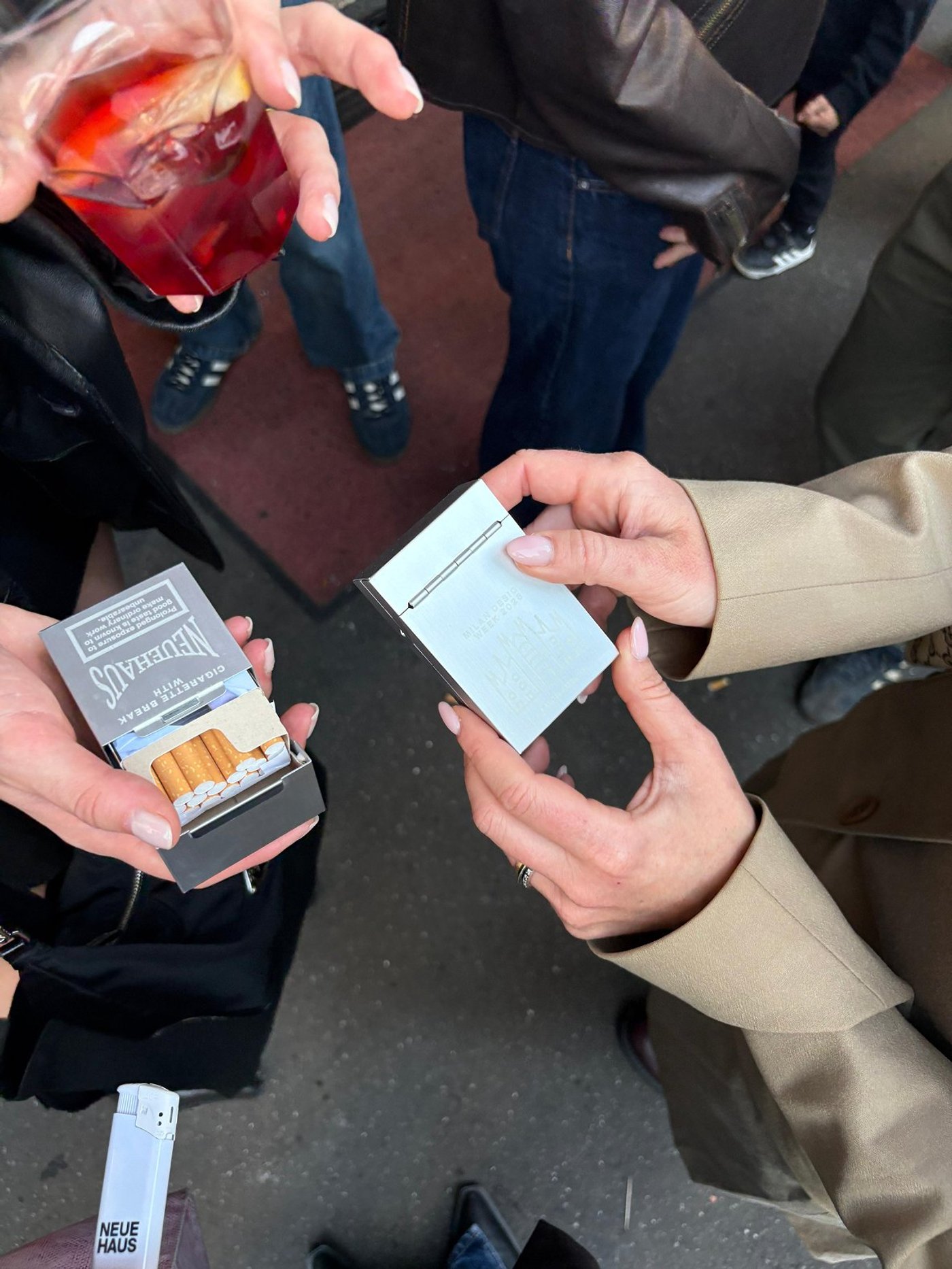 Two people pass a NeueHaus cigarette pack between them at a party.