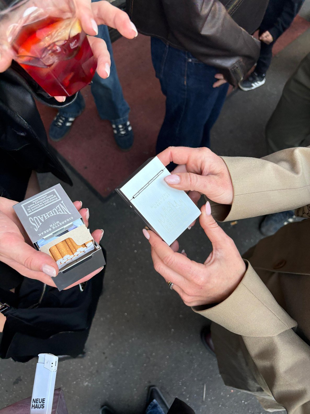 Two people pass a NeueHaus cigarette pack between them at a party.