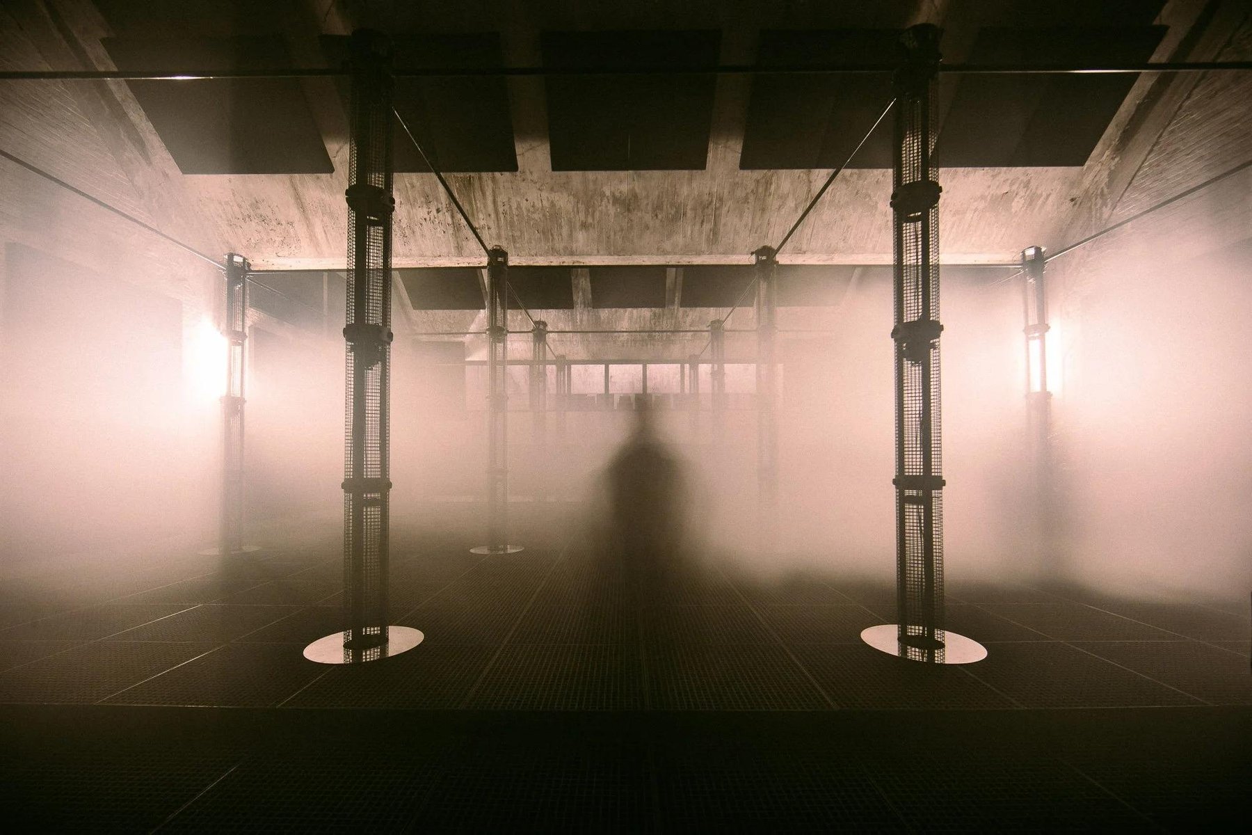 A concrete hall filled with fog, a figure standing in the middle of it.