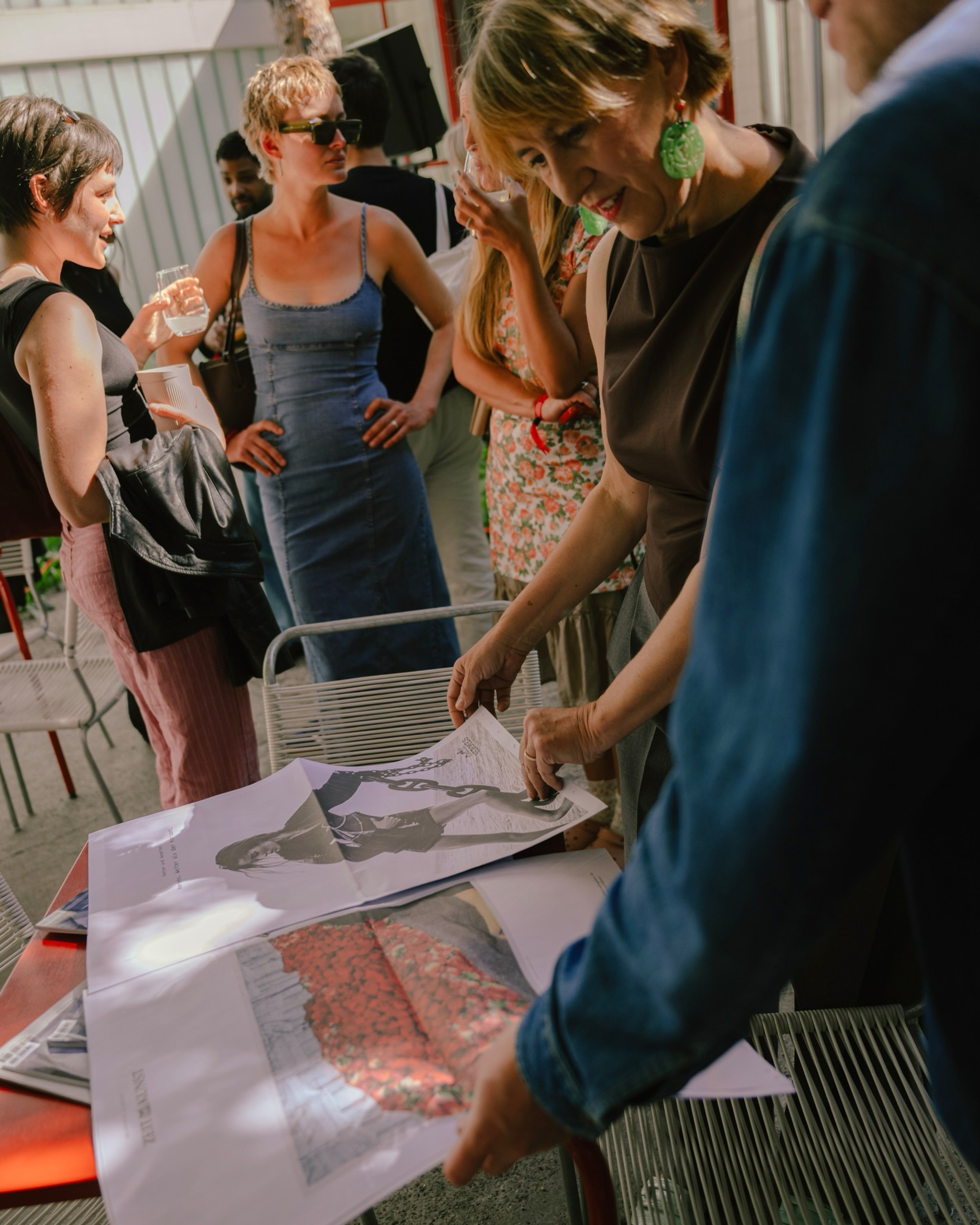 Guests lean over a table of large art prints at a garden gathering.