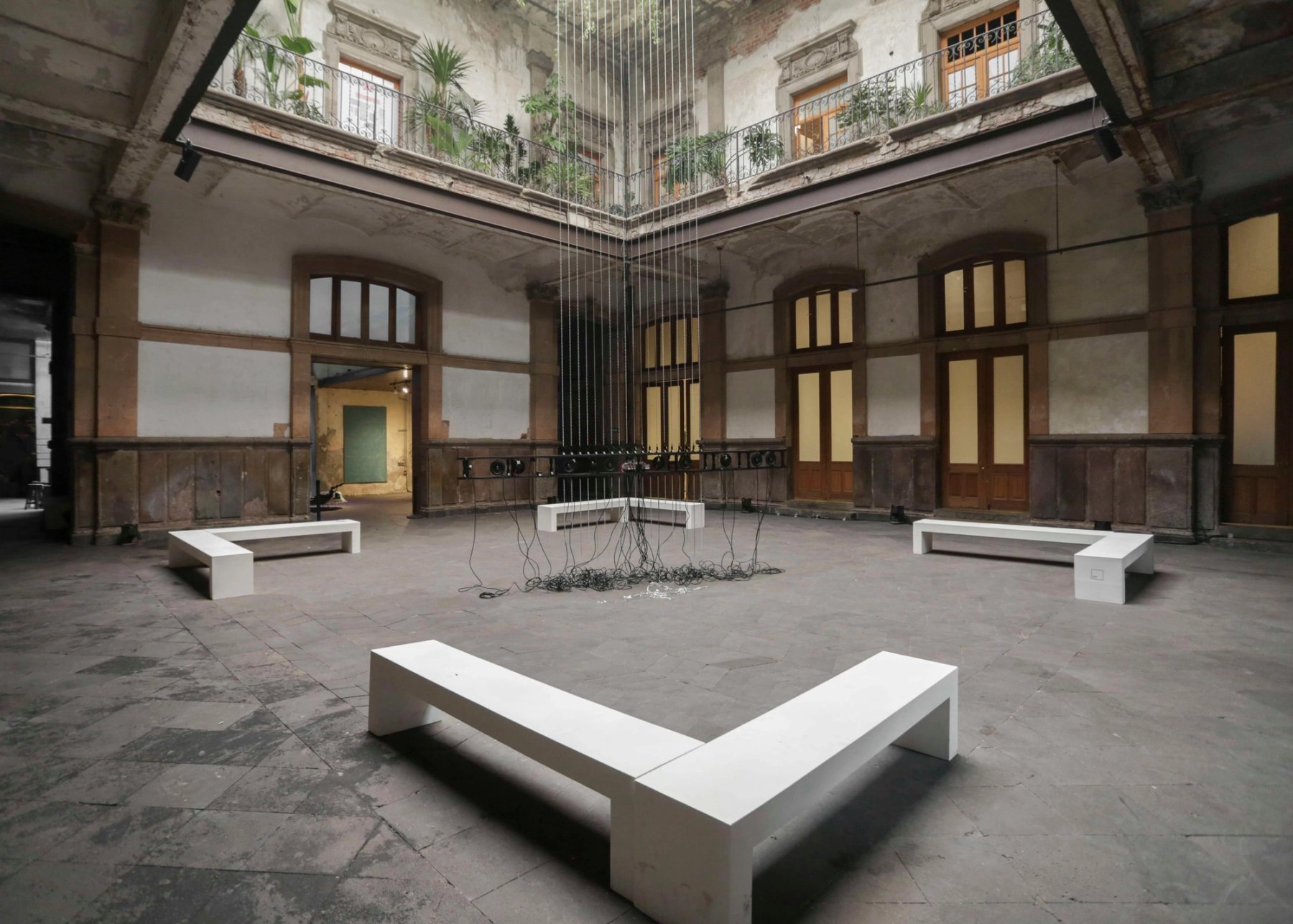A courtyard with white benches and a hanging installation over the stone floor.