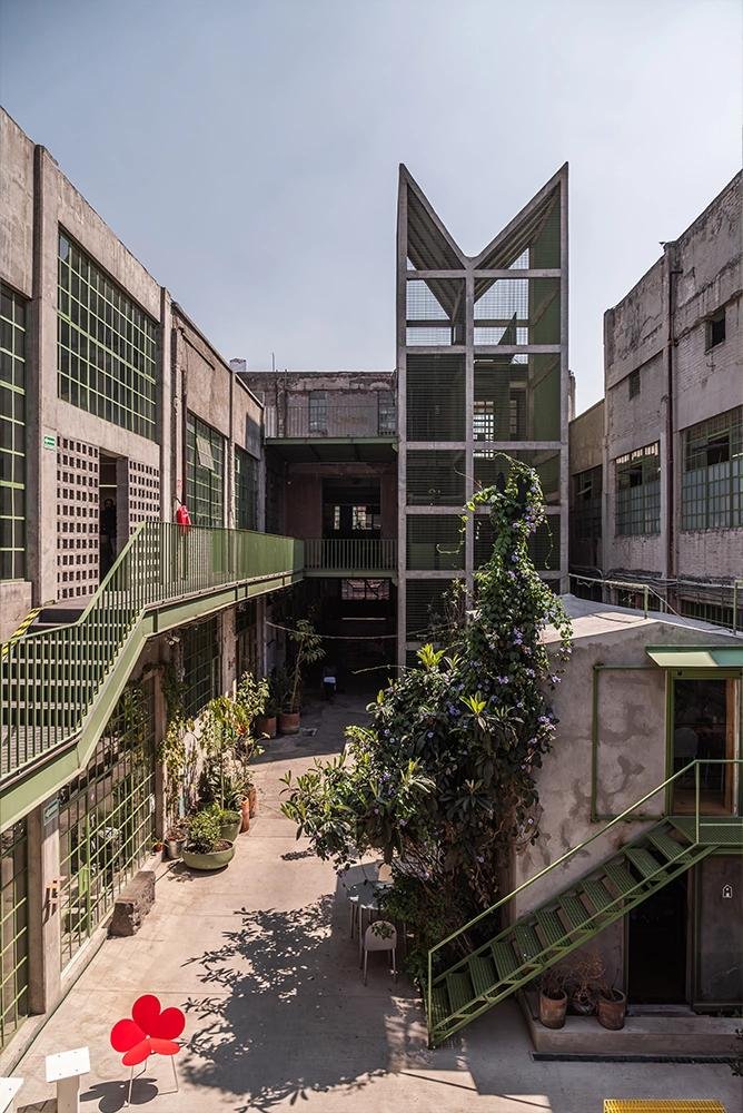 A courtyard in Mexico City with green steel stairs, balconies and plants along the walls.