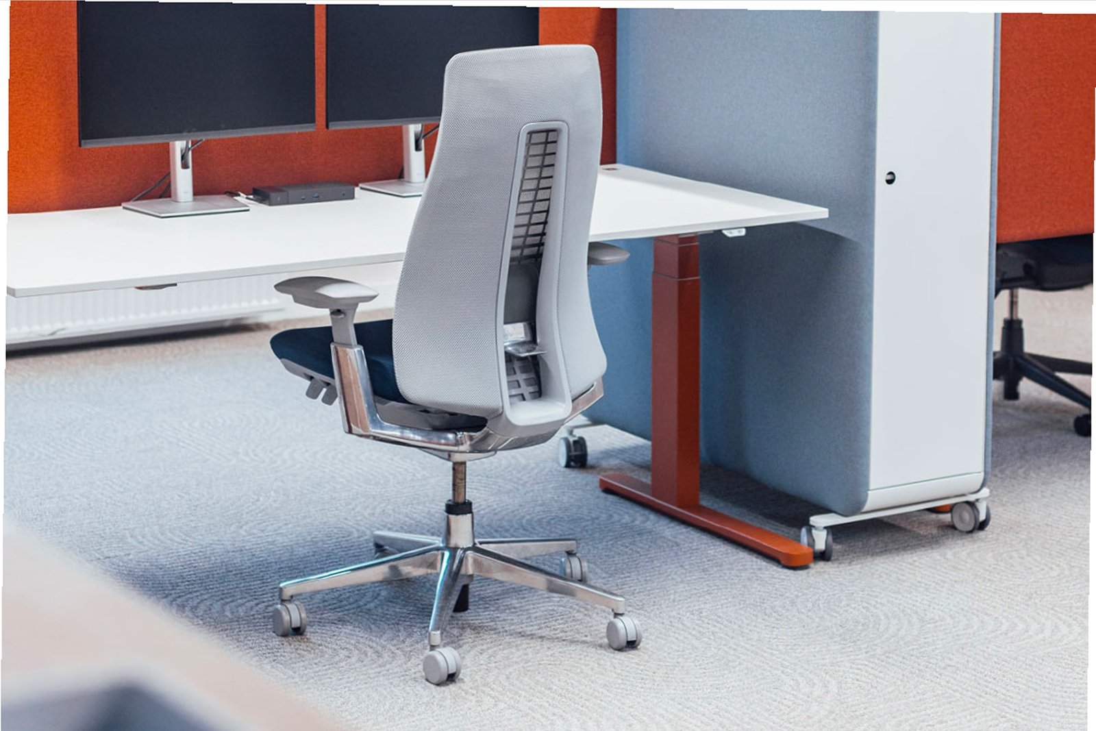 A grey office chair at a desk in an open plan office, with orange screens behind it.