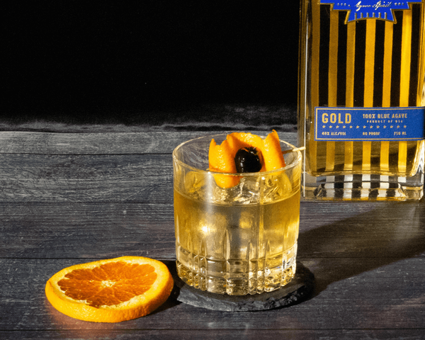 Glass sitting on black coaster with a slice of orange and cherry