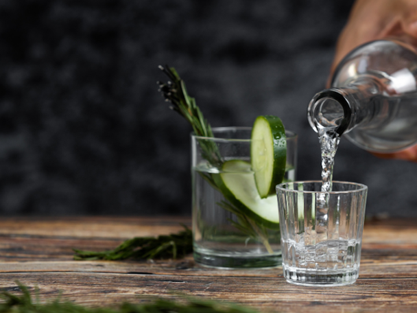 Pouring blanco tequila into a glass another glass in background with blanco tequila with a slice of cucumber