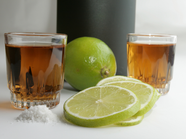 Two glasses of anejo tequila with a lime, limes slices and salt