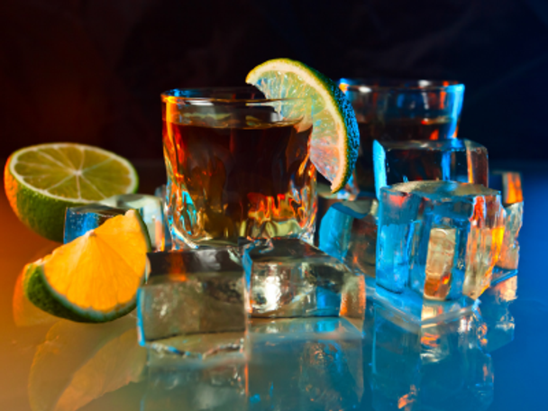 Glass of Extra Anjeo sitting on glass with under-glow lime slices and ice cubes on table